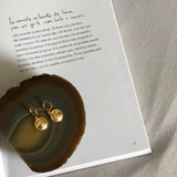 Gold plated Eye coin huggie earrings on a mineral stone and a book