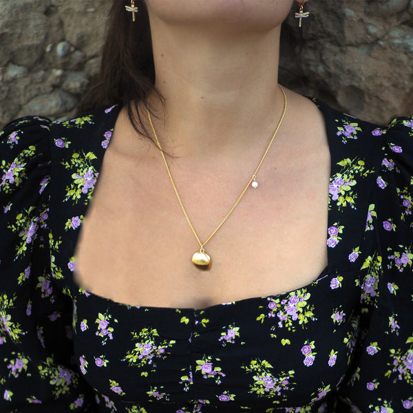 Woman wearing a gold shell necklace and dragon fly earrings
